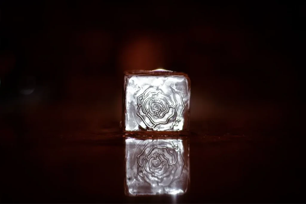 Ice block with carved rose emblem reflecting in dark liquid.