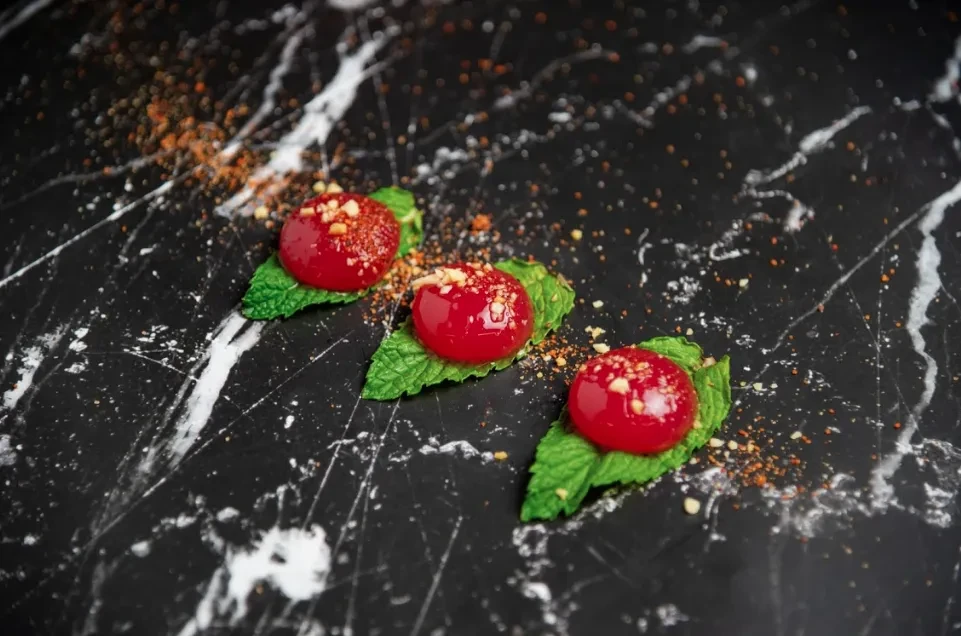Three glossy red spheres with nuts and spice on mint, black marble.