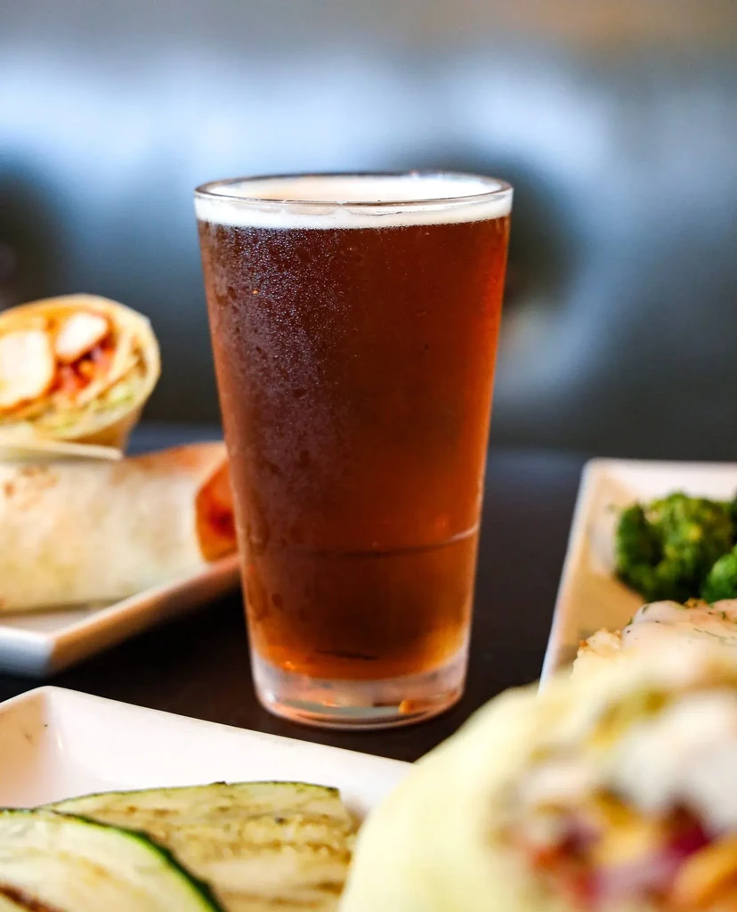 Chilled beer glass surrounded by plates of a wrap, zucchini, and vegetables.