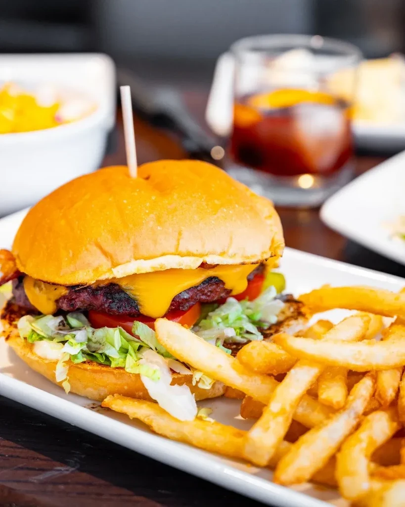 Cheeseburger, golden fries, and cocktail on a dark wooden table.