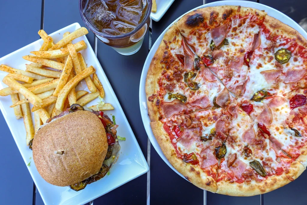 Pizza, burger, fries, and iced drink arranged on a dark table.