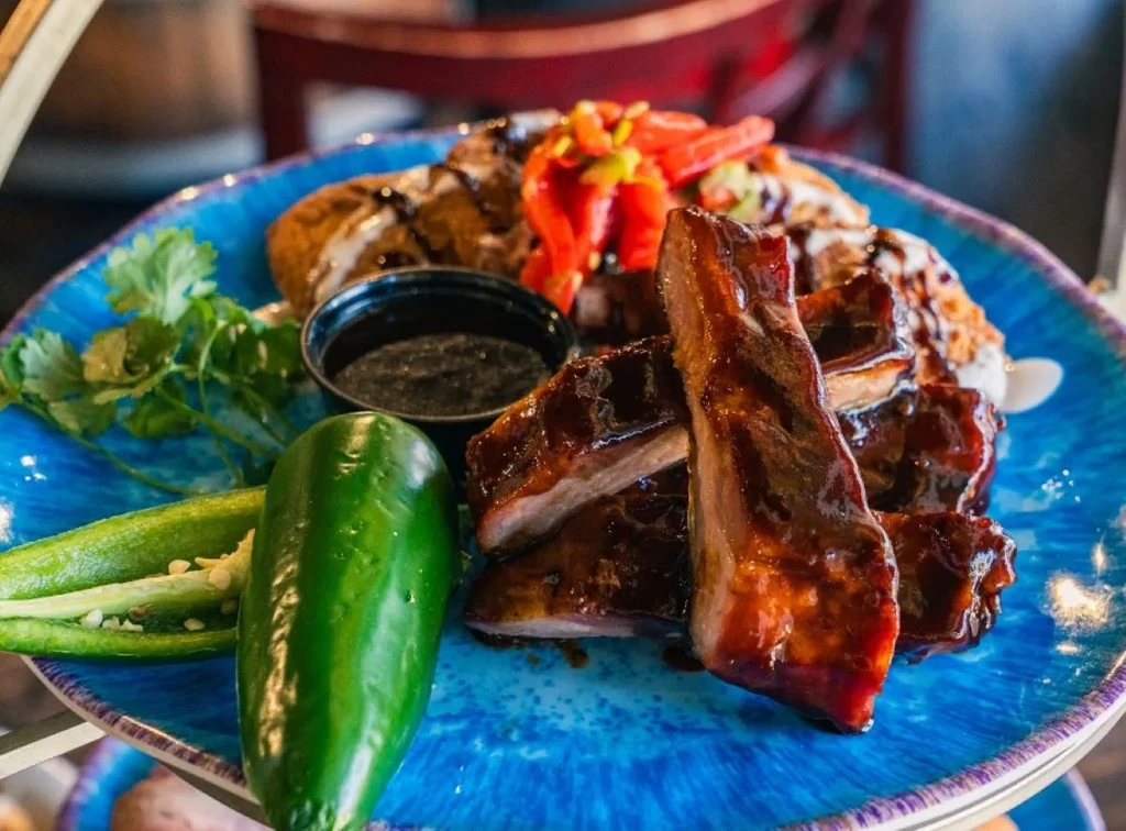 Glazed pork ribs, jalapeño, cilantro, and dumpling on a blue plate.
