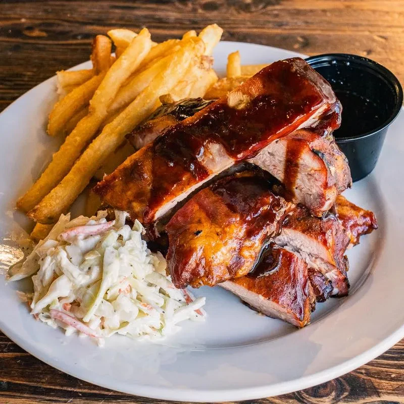 Top-down view of barbecued ribs, french fries, and coleslaw on a white plate.