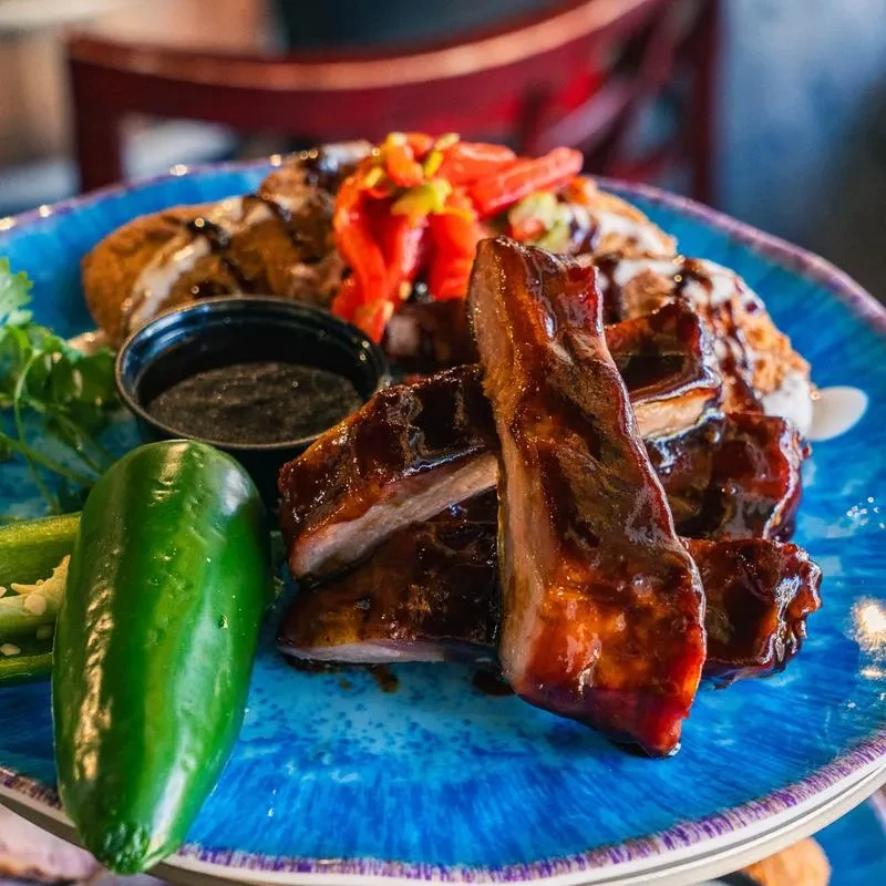 Glazed BBQ ribs, jalapeño, and fried items on a blue plate.