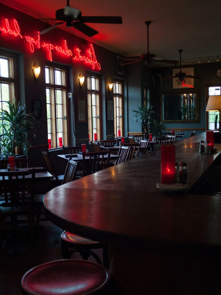Dimly lit restaurant with dark wood furniture and a red neon sign.