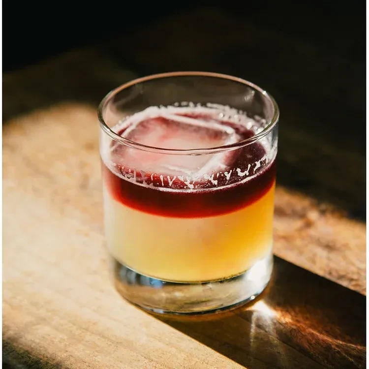 Close-up of a layered cocktail with clear ice on a wooden surface.