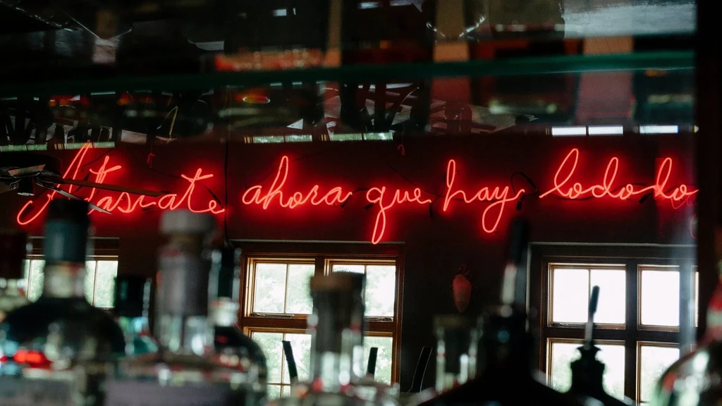Vibrant red neon sign "Atráscate ahora que hay lodo" in a bar.