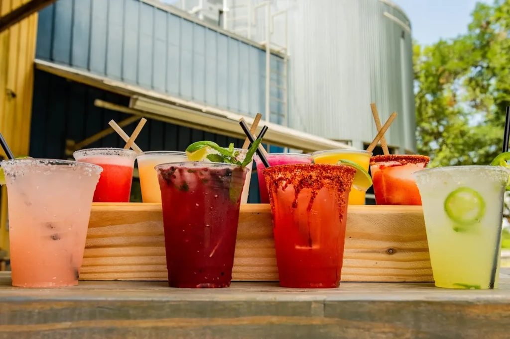 Eight colorful garnished cocktails on wood, industrial background.