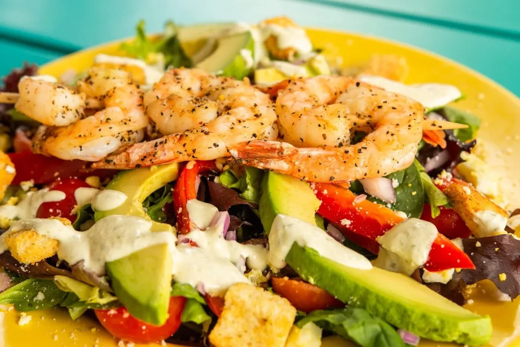 Colorful shrimp salad with avocado, vegetables, and dressing on yellow plate.