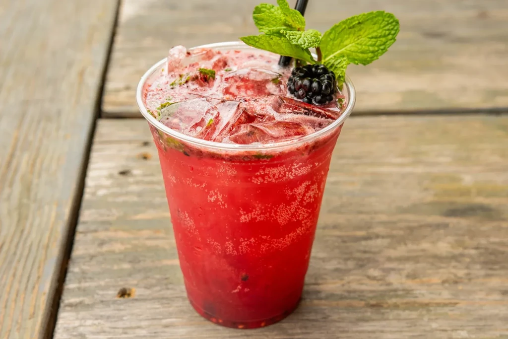 Red iced drink with mint and blackberry on wood.