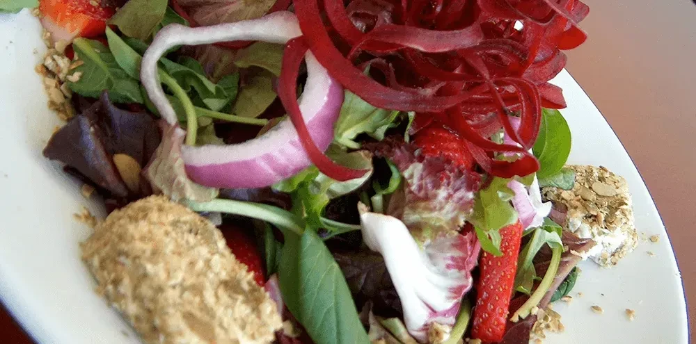 Overhead salad with greens, beetroot, strawberries, and seeded goat cheese.