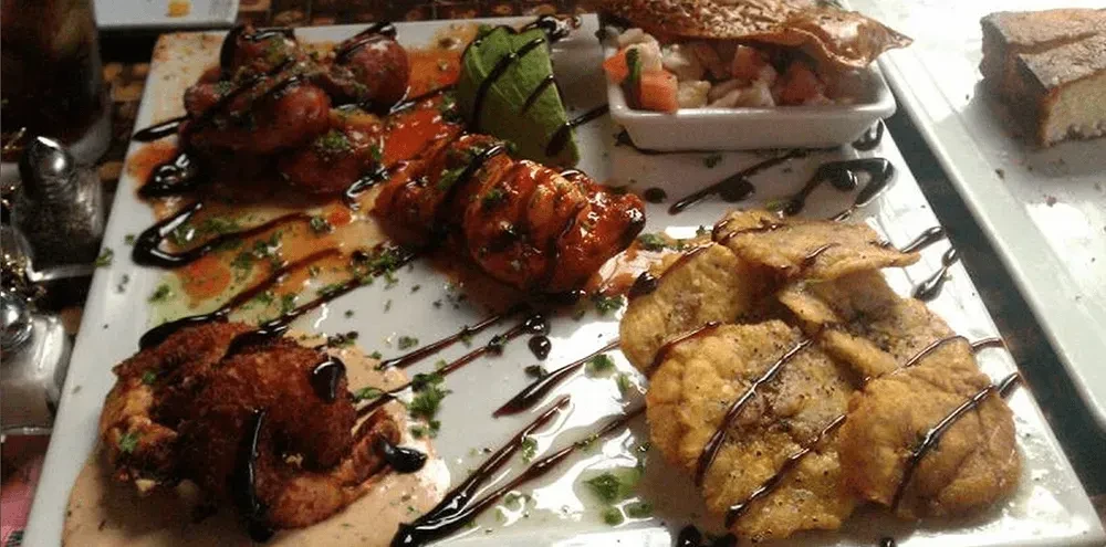 White platter with diverse fried, sauced, and fresh appetizers, garnished with herbs.