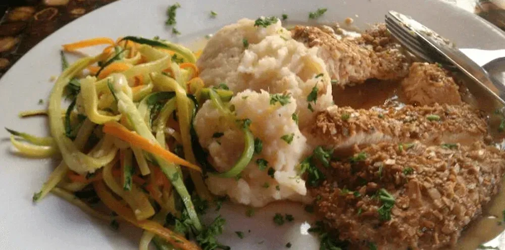 Plated meal: spiralized vegetables, mashed potatoes, crusted protein in sauce.