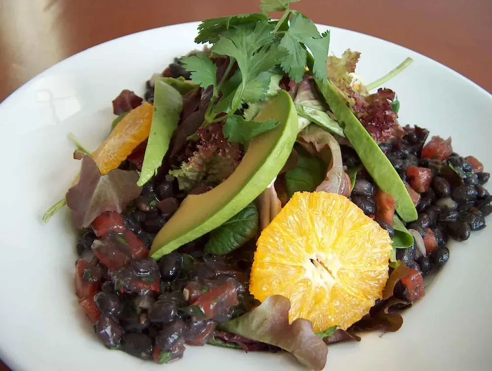 Vibrant black bean salad with avocado, tomato, lettuce, and orange slice.
