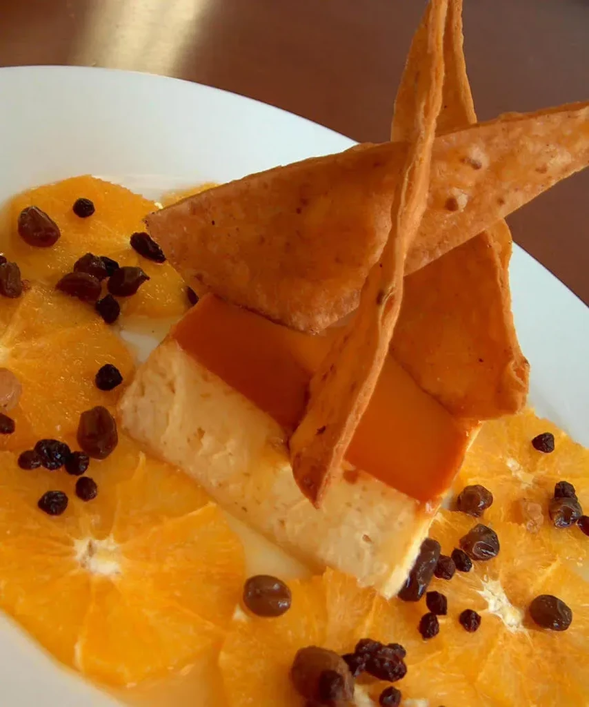 Plated flan with caramelized top, crispy crackers, orange slices, and raisins.