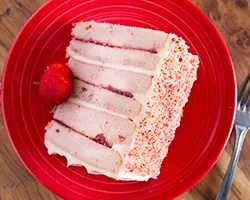 Overhead of layered cake slice, strawberry, and fork on red plate.