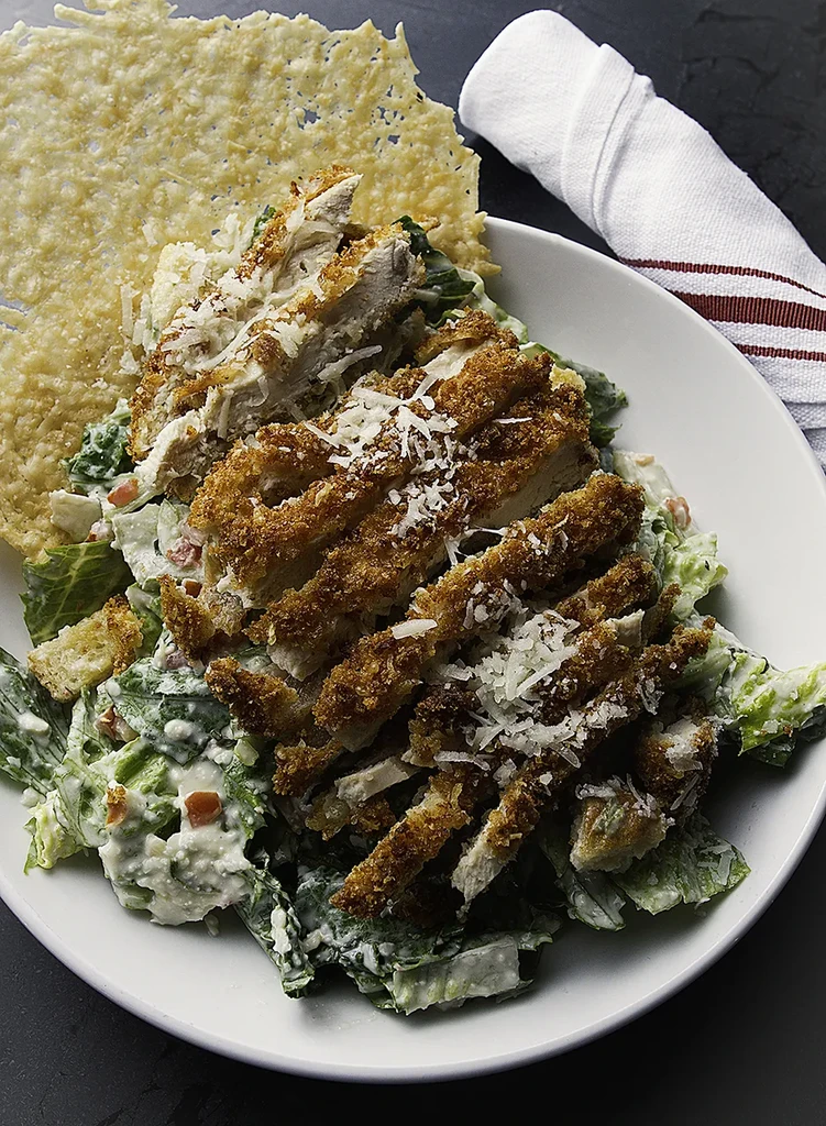 Overhead chicken Caesar salad with crispy chicken and Parmesan crisp.