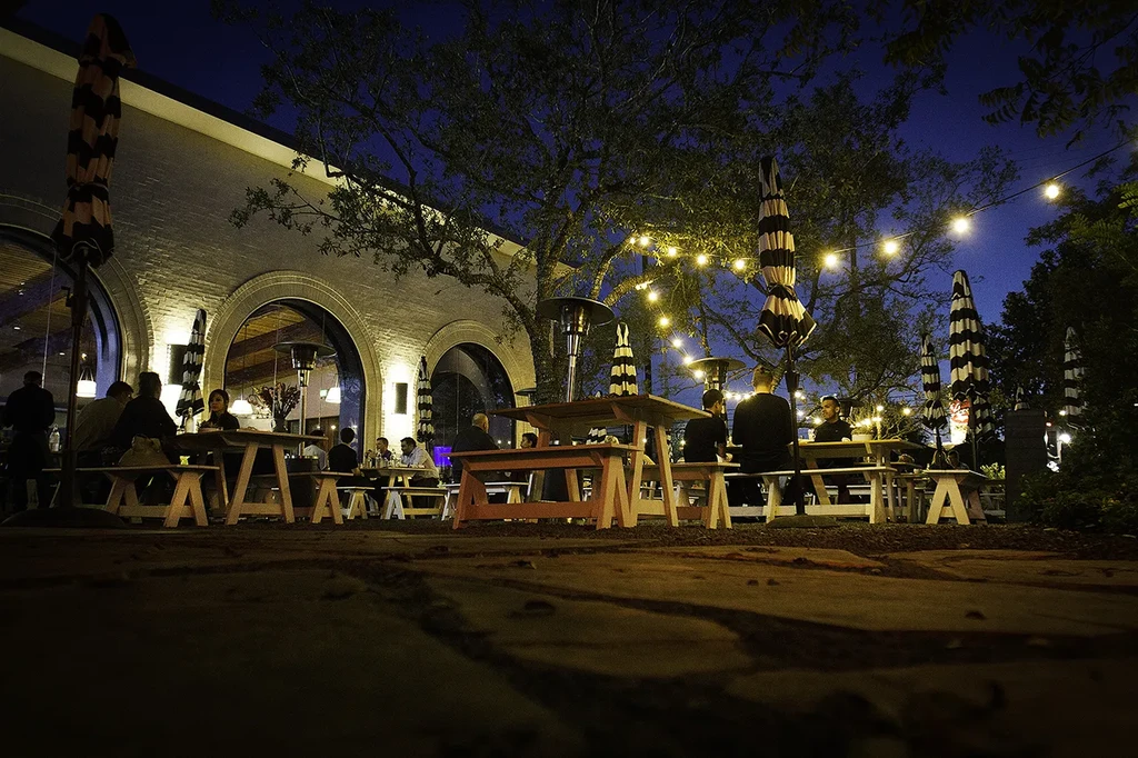 Nighttime outdoor patio with string lights, diners, umbrellas, and heaters.
