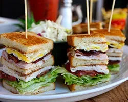 Two quartered club sandwiches featuring meat, fried egg, lettuce, and tomato.