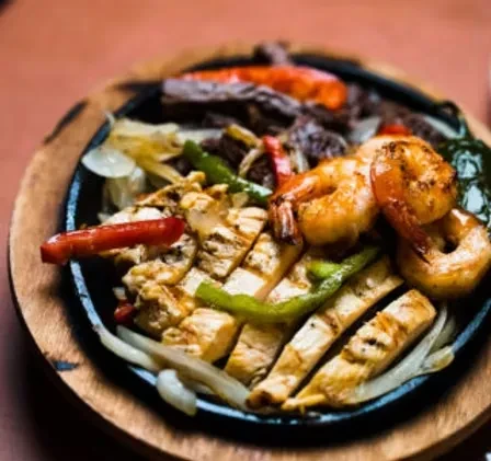 Sizzling fajitas platter with grilled chicken, shrimp, steak, peppers, and onions.