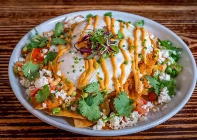 High-angle chilaquiles with sunny eggs, creamy sauce, cheese, and herbs.