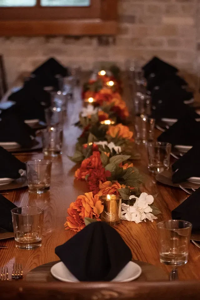 Long wooden dining table with autumnal floral garland and glowing candles.