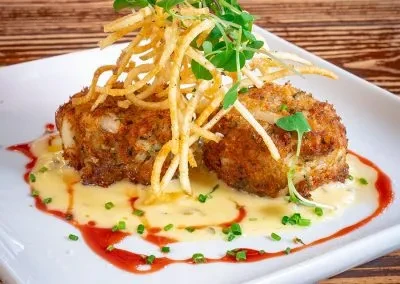 Two golden-brown fried patties with sauces, crispy potatoes, and fresh greens.
