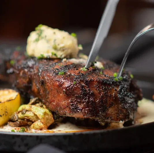 Crusty steak with herb butter, chives, roasted vegetables, and lemon.