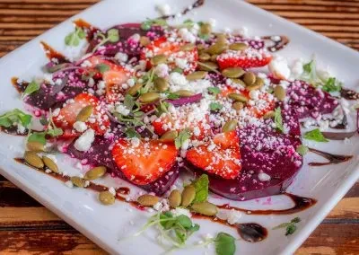 Plated beet and strawberry salad with cheese, pumpkin seeds, and glaze.