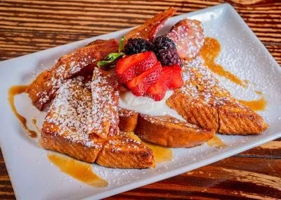 Golden French toast with powdered sugar, berries, cream, syrup, bacon.