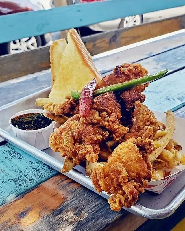 Crispy fried chicken, fries, toast, and greens on a metal tray.