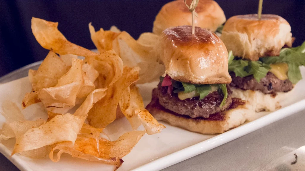 Three sliders with toppings and crispy potato chips on a white plate.