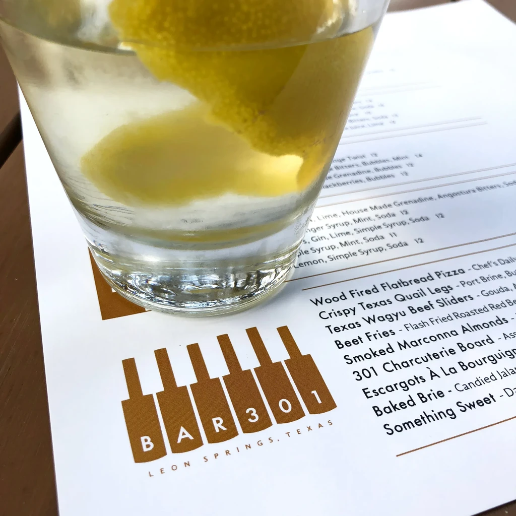 Rock glass with clear drink, lemon, ice, on BAR301 menu.
