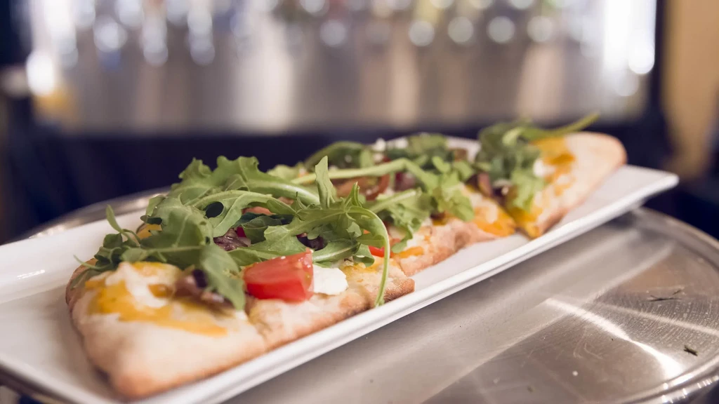Rectangular flatbread pizza with arugula, tomatoes, and melted cheese.
