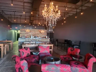 Empty restaurant lounge with patterned chairs, crystal chandelier, and industrial lighting.