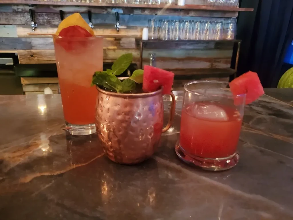 Three distinct garnished cocktails on a marble bar, rustic background.
