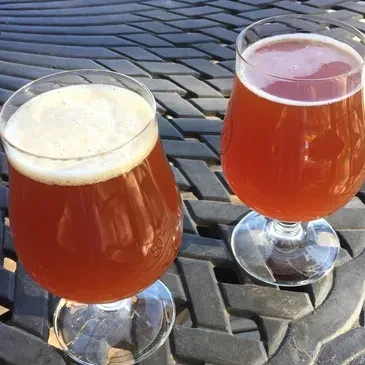 Two stemmed beer glasses, one with more foam, on an outdoor table.