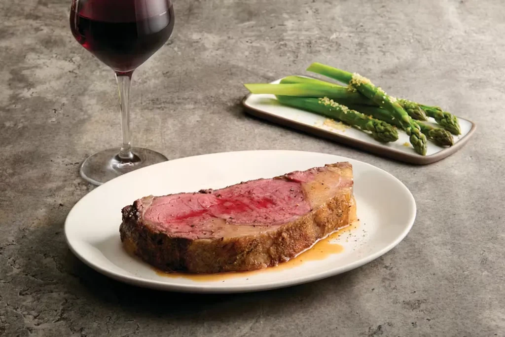 Medium-rare roast beef, red wine, and asparagus on a grey tabletop.