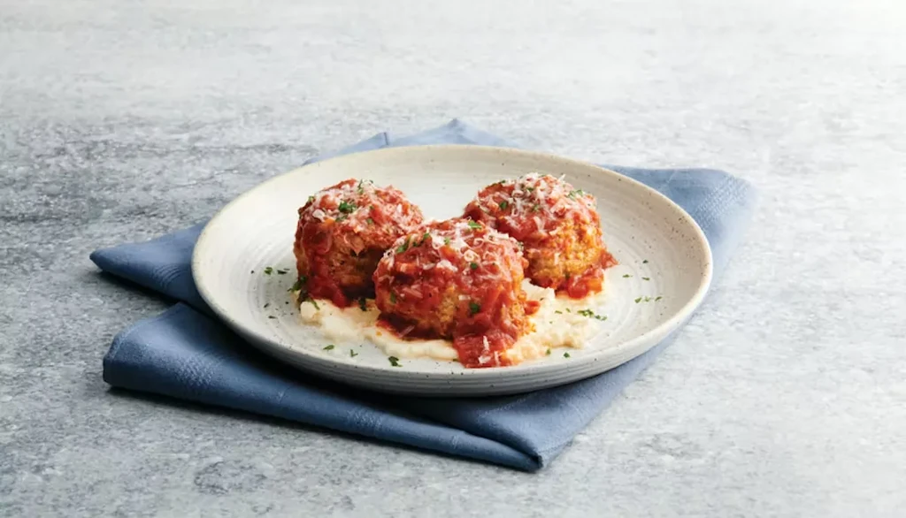 Three meatballs with tomato sauce, cheese, herbs, on creamy purée.