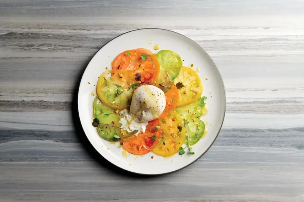 Plated colorful heirloom tomato and burrata salad with olive oil and microgreens.