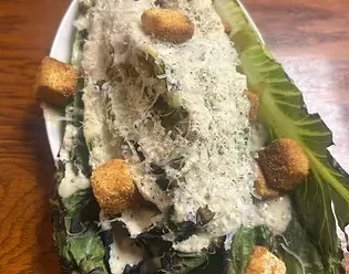 Close-up of grilled Caesar salad with Parmesan, croutons, and creamy dressing.