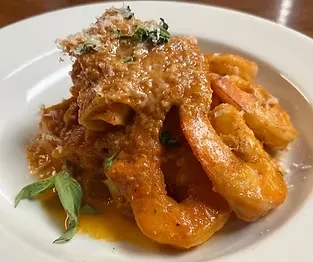 Plate of pasta and shrimp in reddish sauce, topped with cheese and herbs.