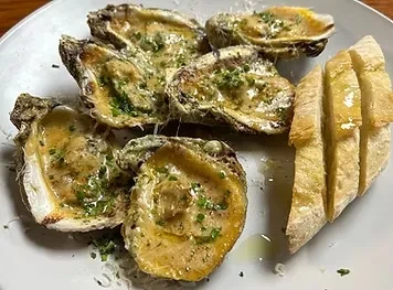 Close-up of six golden-topped baked oysters and crusty bread.