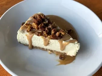 Slice of cheesecake with caramel sauce and crunchy topping on a plate.