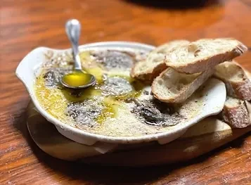 Baked appetizer in gratin dish with golden sauce, herbs, spoon, baguette.