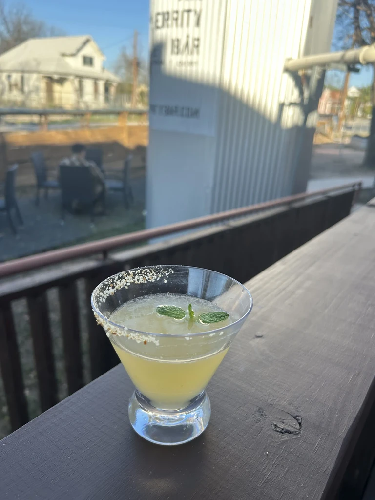 Cocktail with mint and salted rim on a railing, Merritty Bar in background.
