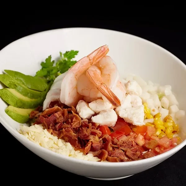 Shrimp salad bowl with avocado, bacon, tomato, cheese, corn, and herbs.