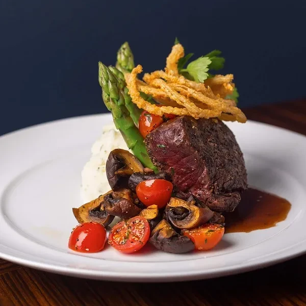 Beautifully plated medium-rare steak with mashed potatoes and vegetables.