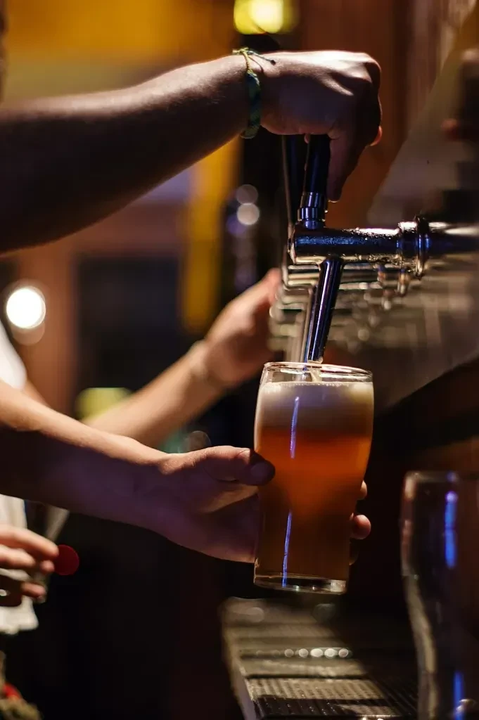 Close-up of hands pouring frothy amber beer from a tap.