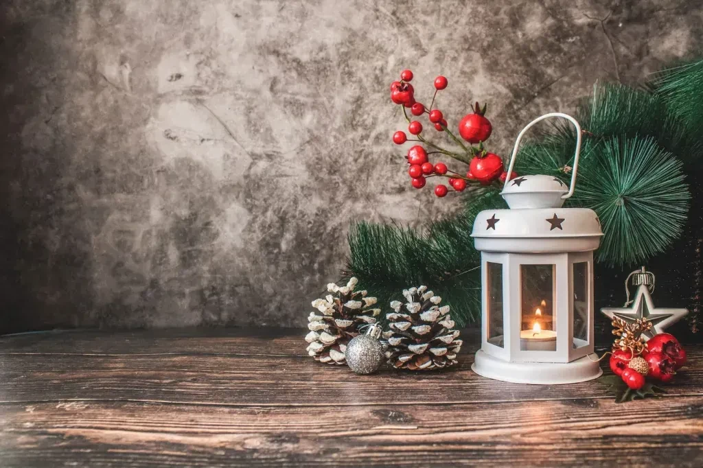 Holiday still life with lit lantern, evergreens, pine cones, and red berries.